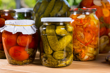 Close Up of Jars of Preserved Vegetables, Freshly Pickled Pickles, Peppers, and Tomatoes on Wooden Tableの写真素材