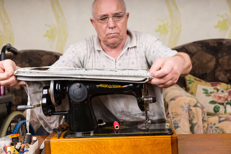 Senior Man at Old Fashioned Sewing Machine Measuring Pant Legs at Home in Living Roomの写真素材