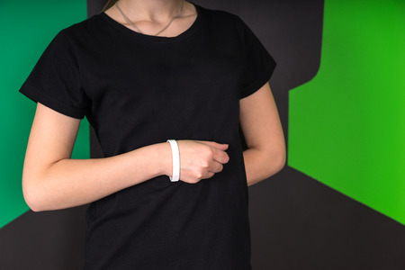 Mid section front view of young female wearing black t-shirt and white wristband, hand in a fist against abdomen, other hand behind back on a green and black background.の写真素材