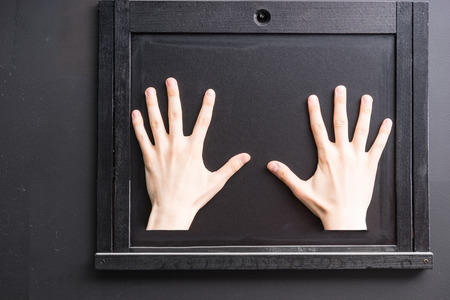 Two hands palm down with fingers spread against black covered wooden window hatch on black wallの写真素材