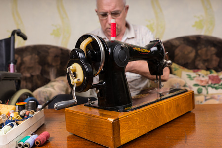 Close Up of Old Fashioned Sewing Machine Surrounded by Various Colorful Threads - Senior Man Behind Vintage Sewing Machine in Living Roomの写真素材