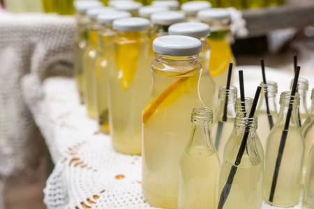 Fresh lemonade in glass bottles with slices of fresh fruit standing on a buffet table at a catered event, some bottles capped, some open with strawsの写真素材