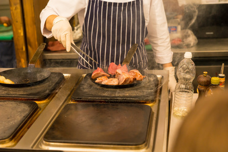 Chef cooking meat over a griddle or commercial hotplate selecting portions of meat with tongs, close up viewの写真素材