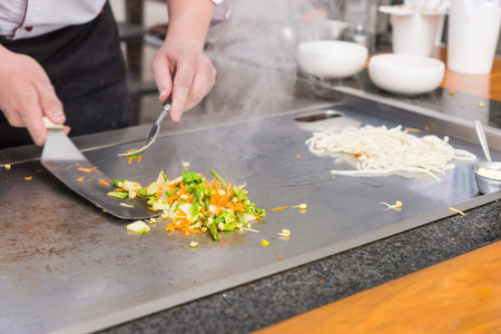 Chef preparing fresh vegetable stir fry over a hot plate turning it with a spatula as he cooks Asian cuisine at a restaurant, close up of his handsの写真素材
