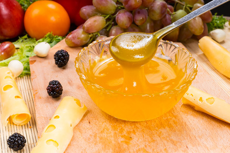 Close Up of Bowl of Fruit Preserves with Spoon on Wooden Board with Cheese and Variety of Fresh...