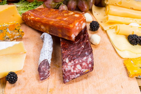 Variety of Smoked and Cured Gourmet Meats on Wooden Board with Cheeses and Fresh Fruit - Appetizing Gourmet Food Still Lifeの写真素材