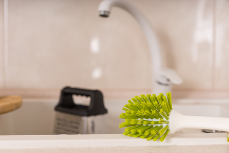 Close Up of Green Scrub Brush Resting on Edge of Kitchen Sink, Ready to Wash Dirty Dishes Following Meal Preparationの写真素材