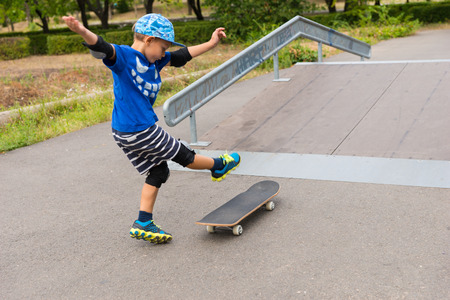 Full Length of Enthusiastic Young Boy Kicking Foot Up at Skateboard at Bottom of Ramp in Skate Park on Summer Dayの写真素材