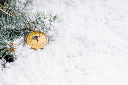 New Year background with green pine branches and a vintage yellow clock on white snow at midnightの写真素材