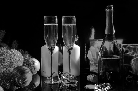 Festive Black and White Still Life - Two Glasses of Sparkling Champagne on Table with Candles, Gifts, Pocket Watch and Christmas Decorationsの写真素材