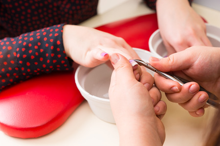 Close Up of Hands of Female Manicurist Trimming Cuticles of Female Client Wearing Polka Dot Blouse in Salonの写真素材