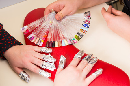 High Angle Close Up View of Female Client with Nails Wrapped in Foil During Gel Manicure with Manicurist Displaying Samples of Patterns During Gel Manicureの写真素材