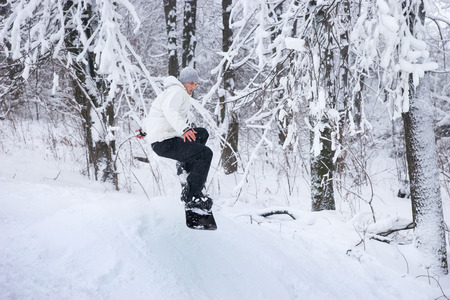 Young man snowboarding in fresh white snow alongside a line of bare winter trees as he demonstrates his skillの写真素材