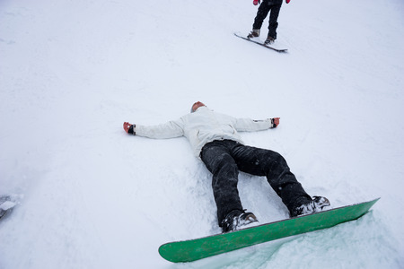 Snowboarder lying prone on his back with outstretched arms in the winter snow wearing his green snowboard, conceptual image with copy spaceの写真素材