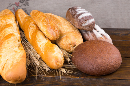 Set of rye and white artisan breads piled with stalks of dried wheat on dark wooden tableの写真素材
