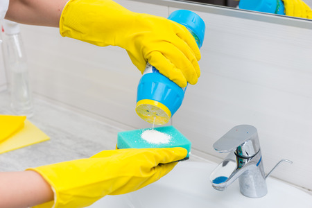 Woman scrubbing the hand basin in the bathroom using an abrasive powder and sponge under running...