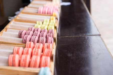 Trays filled with colorful macaroons or French macarons on a counter in a bakery or market with selective focus to purple berry flavored cookiesの写真素材