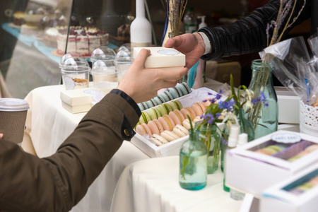 Woman purchasing a French macaron at a market stall being handed a small box by the vendor, close up of their handsの写真素材