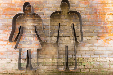 Metal silhouette cut out sign of a man and woman on an old exterior weathered brick wall standing side by sideの写真素材