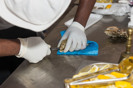Close Up of Unrecognizable Man Hands Shucking Oysters Shellfish at Restaurant Buffet or Food Festivalの写真素材