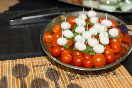 Tray of fresh Capresi salad with whole fresh tomatoes, basil leaves and mozzarella cheese on toothpicksの写真素材