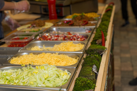 Close Up Still Life of Variety of Garnishes for Mexican Food Chilling in Trays at Food Festival Cart with Person Preparing Tortilla in Backgroundの写真素材