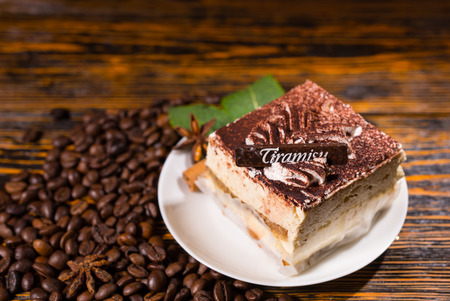 Delicious square shaped cake slice in plate surrounded by coffee beans over dark stained wooden backgroundの写真素材