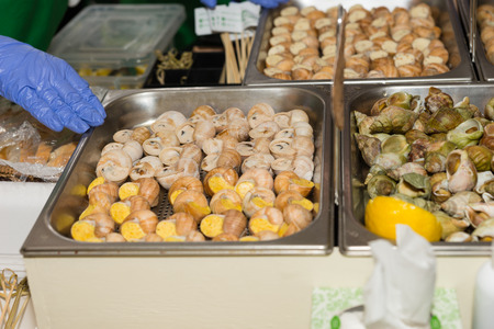 Trays of assorted stuffed snails with different flavored fillings on display at a market or buffet in stainless steel traysの写真素材