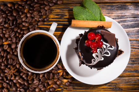 Overhead view of coffee beans beside white mug and dessert decorated with chocolate and red berries on a wood tableの写真素材