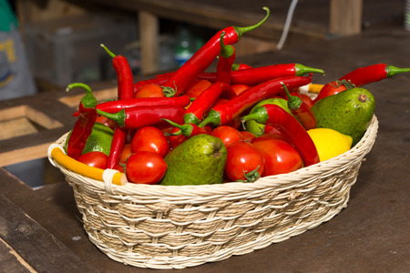 Colorful woven wicker basket of fresh fruit and vegetables with hot chili peppers, avocado pear and lemonの写真素材
