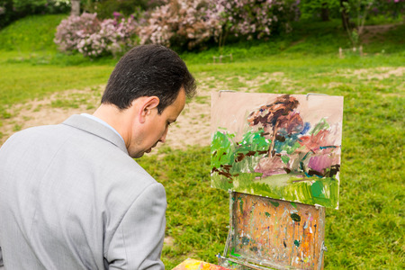 Male handsome middle-aged creative artist  standing in front of a sketchbook during an art class in a outdoorsの写真素材