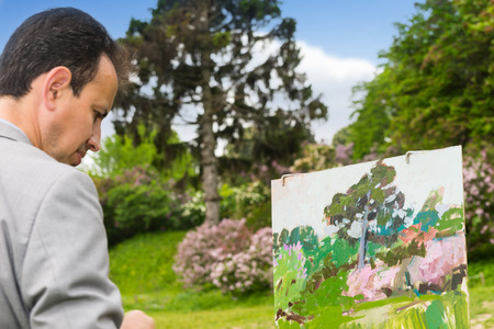 Portrait of a handsome fashionable male artist working outdoors in the park or garden on a trestle and easel painting with oils and acrylics during an art classの写真素材