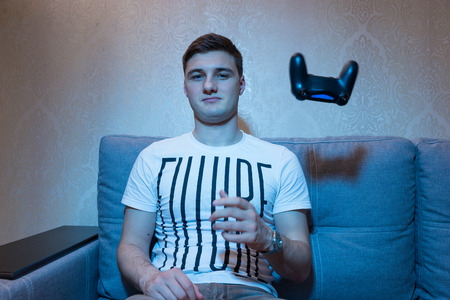 Male gamer throw away  a console after playing a game sitting in front of the television on the sofa...