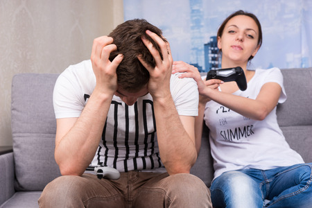 Young and trendy girl gloating after winning a video game pointing at her husband with a smile as he...