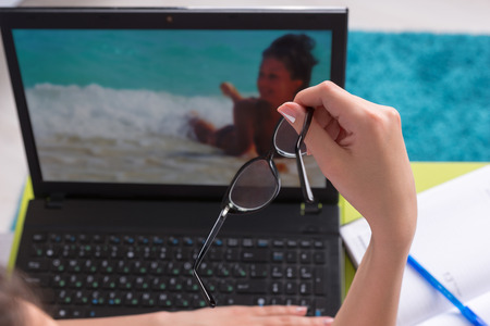 Female worker working on a laptop computer holding a pair of eyeglasses in her hand as she surfs the...