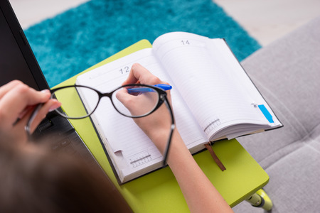View through glasses to the open blank page of a business journal or diary with a woman's hand, who holding a pen for making appointments, organising a schedule or agendaの写真素材