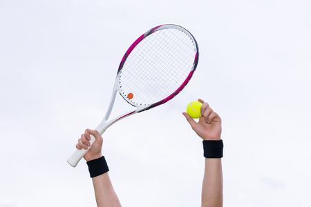 Human hands with wristbands holding tennis ball and a racket on background of the skyの写真素材