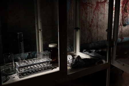 Stained laboratory with test tubes holder and other medicine devices inside with blood spattered wall in dark room in a Halloween horror conceptの写真素材