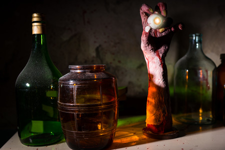 Close up of wrinkled hand with eyeball between glass jars with blood spattered wall in a Halloween horror conceptの写真素材