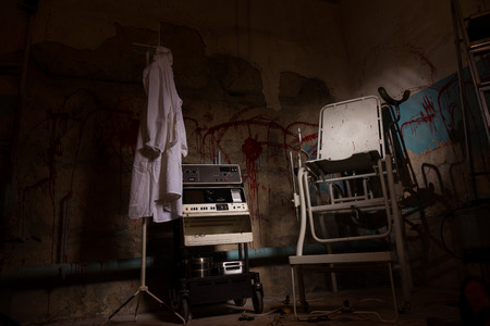View of electrical shocking device near medical gown hanging on the hanger and scary chair with...