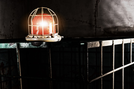 Shining red lamp on the iron cage behind blood splattered wall for concept about torture or scary Halloween themeの写真素材