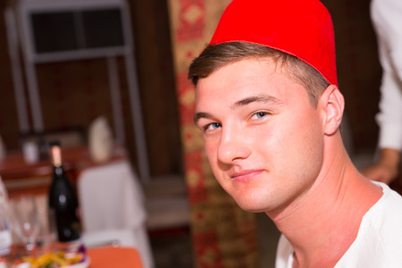 Handsome young man sitting in Moroccan restaurant and celebrating something, wearing fezの写真素材