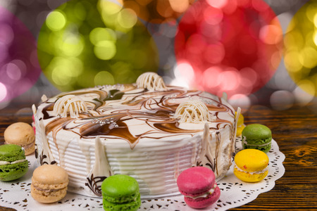 Close up of cake with chocolate ornaments, near macarons, on colorful brighting background