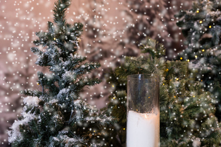 Close up of big candles in glass vases near fir-tree with flashlights in a snow-covered park or a forest while snowingの写真素材