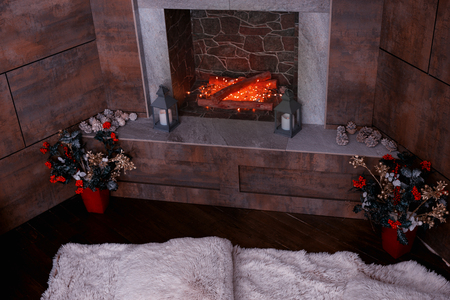 Decorated modern fireplace with candles, fir-cones in the living room with white furry rug and vases with artificial flowersの写真素材