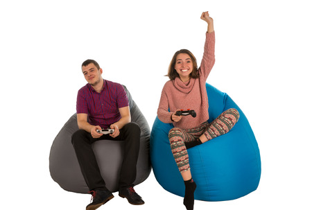 Young man and woman are enthusiastic about playing video games while sitting on blue and grey beanbag chairs for living room or other room isolated on white backgroundの写真素材