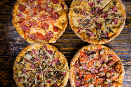 High angle view of four different delicious pizzas on wooden tableの写真素材