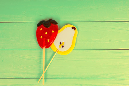 Tasty lollipops as a pear and strawberry on wooden green boardの写真素材