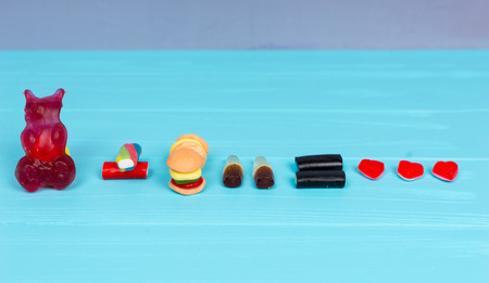 Tasty candies represent in the form of a gummy bear, burger and drink that is love on wooden turquoise tableの写真素材