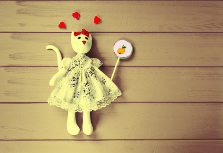 Monochrome image of homemade toy in the form of a cat with gummy hearts around holding lollipop on wooden boardの写真素材